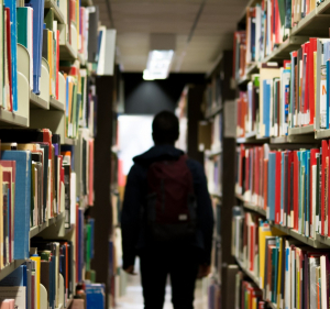 Photographie d'un étudiant de dos au milieu des rayons d'une bibliothèque